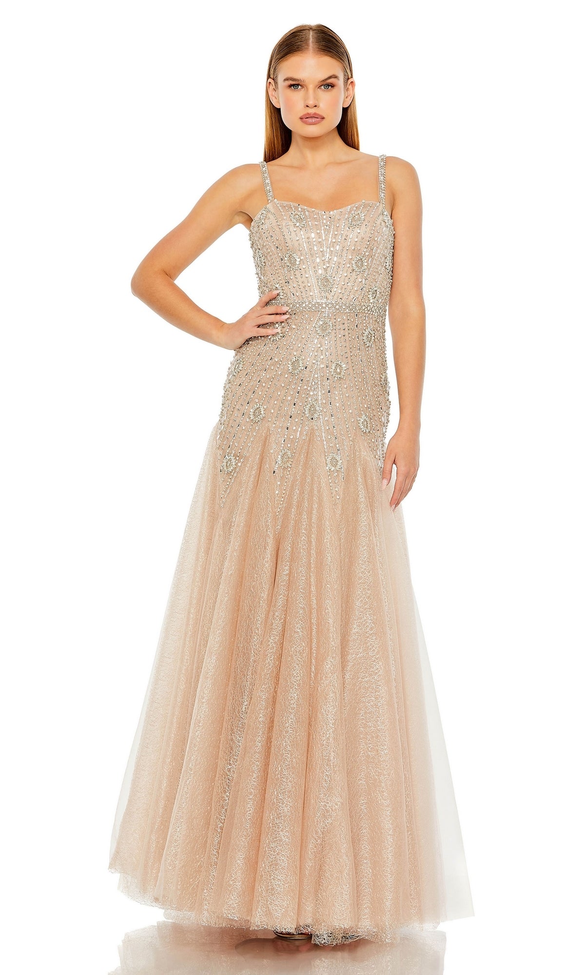A woman poses with one hand on her hip, wearing the Long Formal Dress 2236 by Mac Duggal—an elegant, sleeveless champagne A-line gown adorned with sparkling beads and sequins.